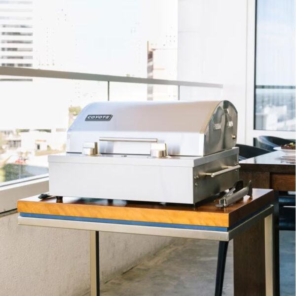 Coyote stainless steel grill on a modern outdoor table with a city view, perfect for outdoor cooking and entertaining.