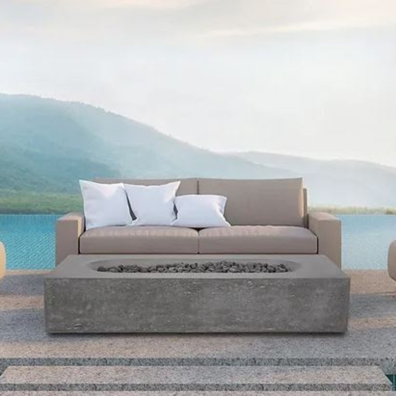 Modern outdoor seating area featuring a beige sofa with white pillows and a concrete fire pit, overlooking a serene lake and mountains in the background. Ideal for relaxation and gatherings.