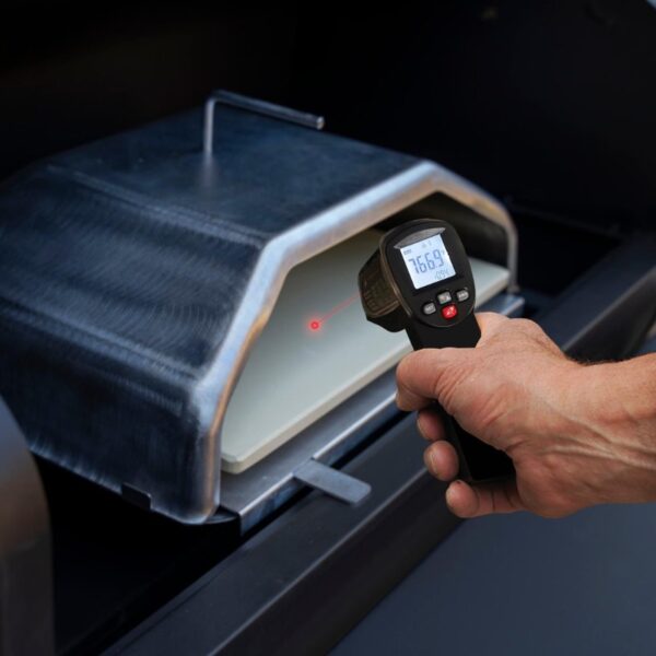 Hand holding an infrared thermometer measuring the temperature inside a grill, displaying a reading of 766.9°F on the digital screen.