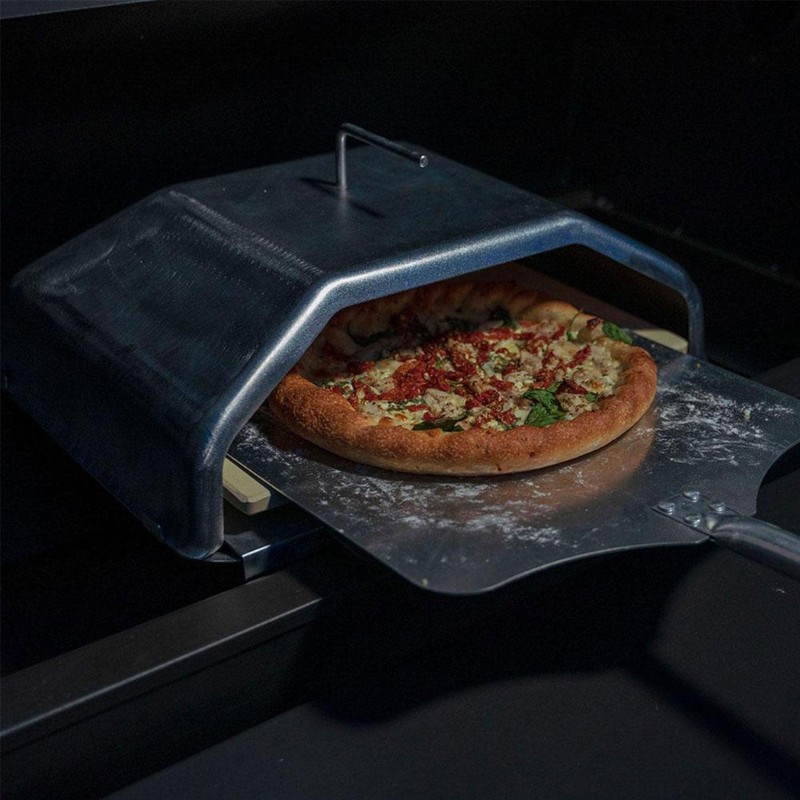 Metal pizza oven with a freshly baked pizza topped with sun-dried tomatoes and spinach on a pizza peel.