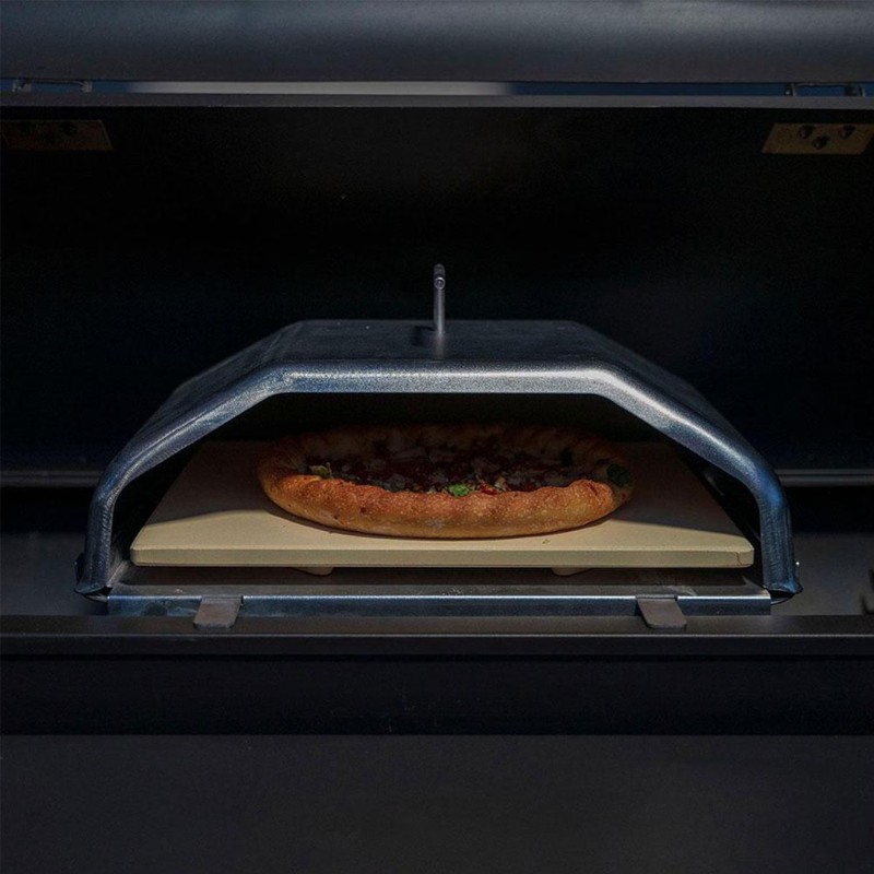 Pizza baking in an oven with a metal cover and a stone baking surface, showcasing a golden crust and toppings.