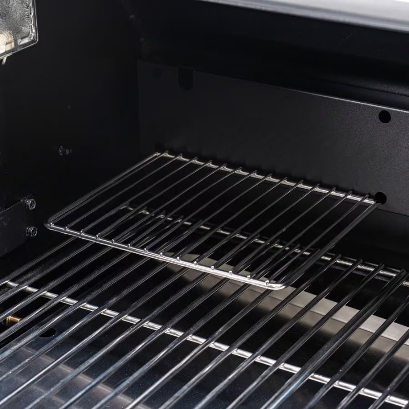 Interior view of a gas grill showcasing stainless steel cooking grates and adjustable shelf for optimal grilling and cooking versatility.