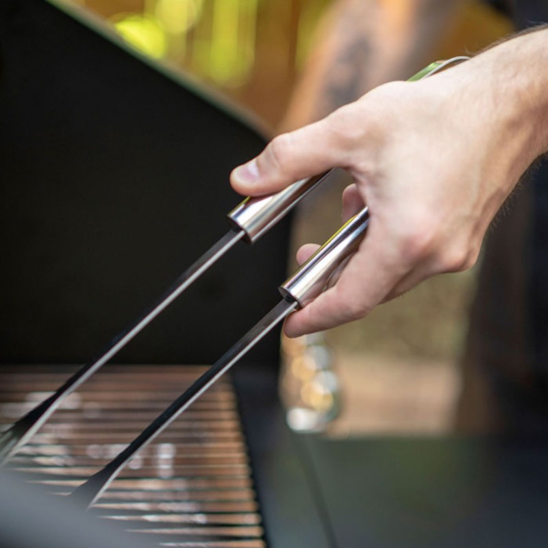 Hand holding stainless steel grilling tongs over a barbecue grill, ready to flip or serve food.
