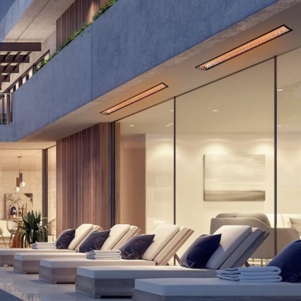 Modern outdoor lounge area with reclining chairs and plush cushions, featuring a sleek glass wall and stylish heating lamps for comfort.