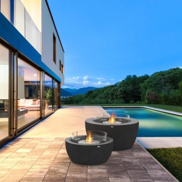 Modern outdoor living space featuring two stylish fire pits beside a swimming pool, with a contemporary home and lush greenery in the background.