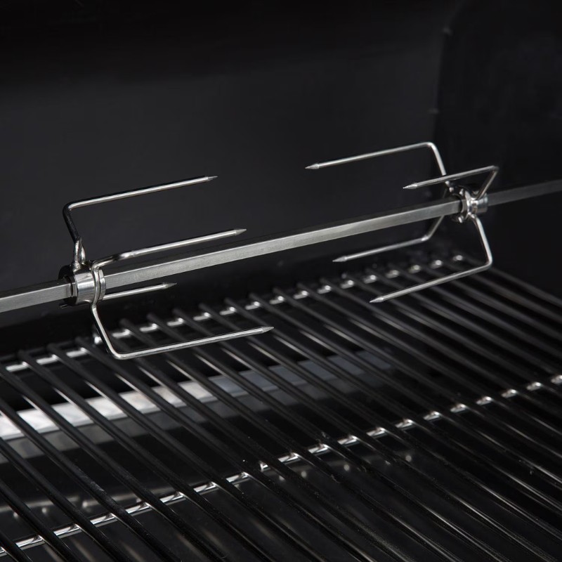 Stainless steel rotisserie fork and spit rod resting on a grill, designed for even cooking of meats.
