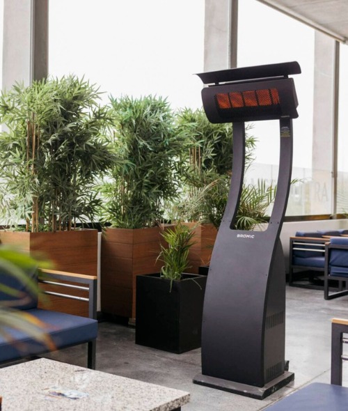 Outdoor electric patio heater beside lush greenery in a modern seating area.