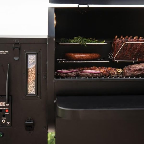 Close-up of a modern smoker grill showcasing various meats, including ribs, sausage, and burgers, with smoke wood pellets visible in the side compartment.