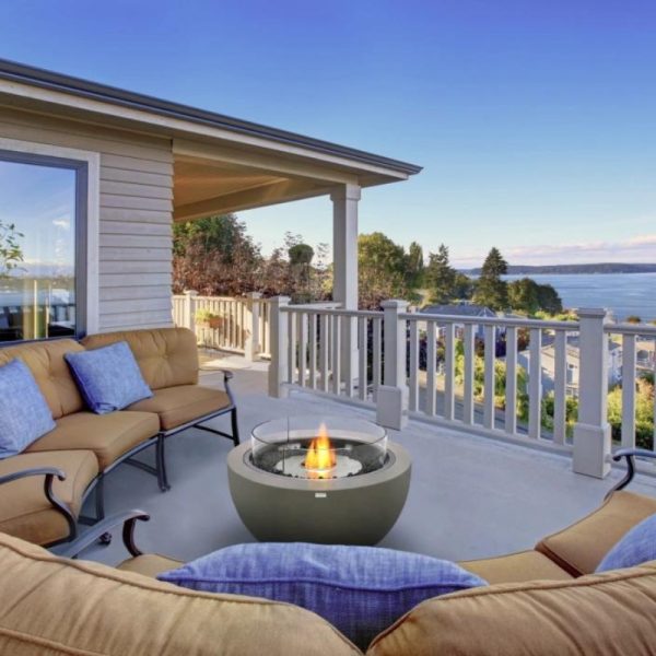 Cozy outdoor seating area featuring a modern fire pit, overlooking a scenic waterfront view with clear blue skies.