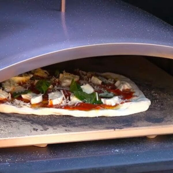 Pizza with fresh toppings, including sauce, cheese, and basil, baking in a pizza oven.