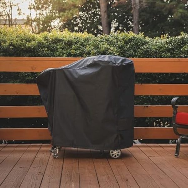 Black outdoor grill cover on a wooden deck, with greenery in the background, providing protection from the elements.