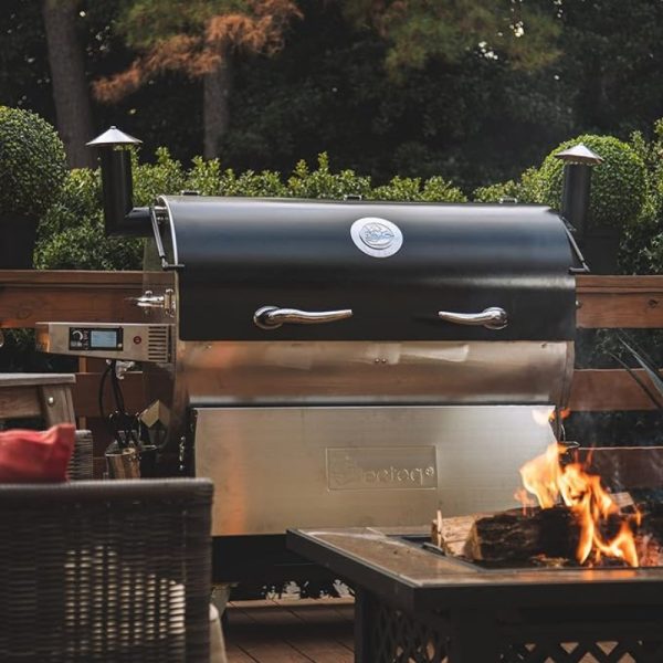 Outdoor pellet grill with a sleek black design, stainless steel accents, and a fire pit in the foreground, set in a backyard environment.