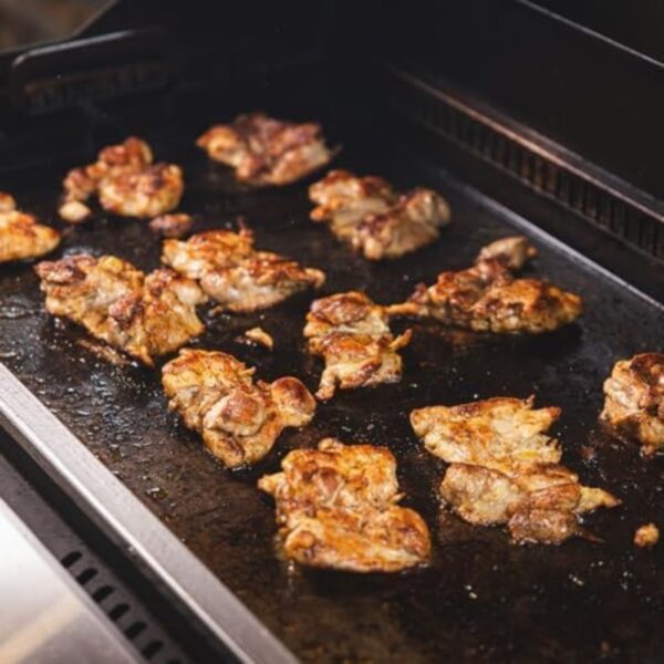 Grilled chicken thighs sizzling on a hot griddle, showcasing a golden-brown sear and juicy texture.