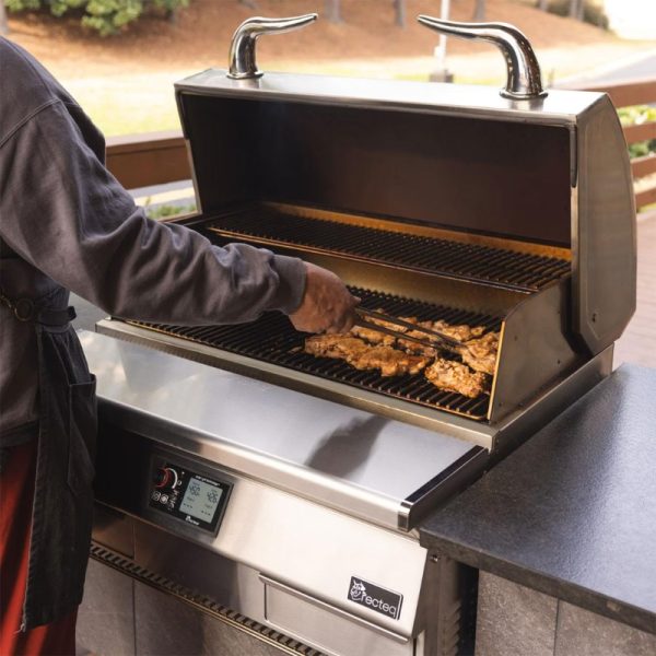 Person grilling chicken on a stainless steel outdoor grill with tongs, showcasing a modern grilling setup and cooking process.