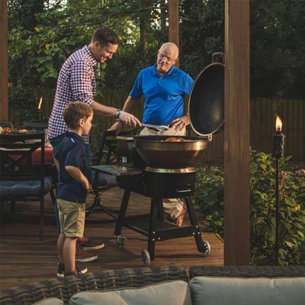 Family members enjoying a barbecue on a patio, with a grandfather and father grilling while a young boy observes, surrounded by greenery and outdoor seating.