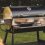 Black outdoor pellet grill with stainless steel accents, featuring a cooking surface and side dishes on a table.