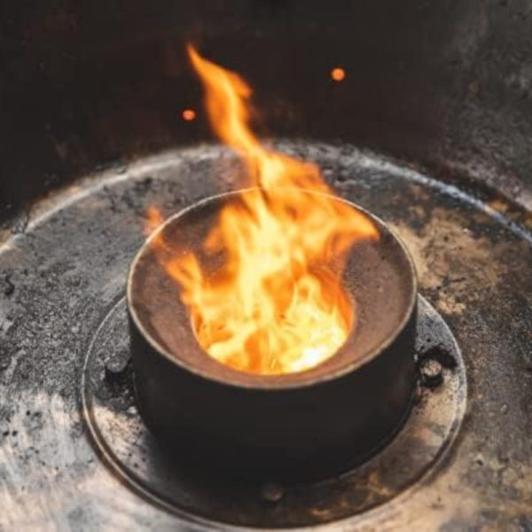 Flames erupting from a circular metal burner in a dark, industrial setting, showcasing intense heat and energy.