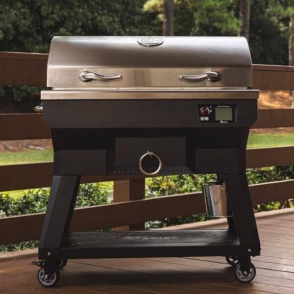 Black outdoor grill with a stainless steel lid, digital controls, and storage space, positioned on a wooden deck surrounded by greenery.