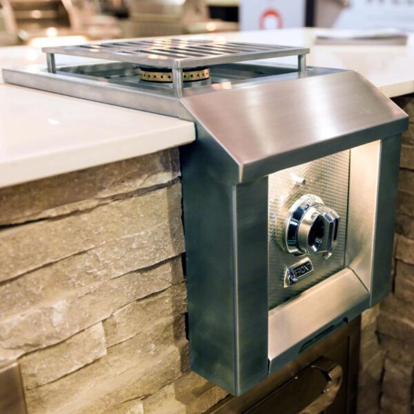 Stainless steel outdoor gas grill integrated into a stone countertop, featuring a control knob and illuminated design for modern cooking spaces.
