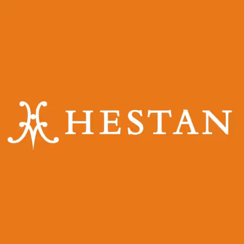 Hestan brand logo on an orange background, representing high-quality cookware and kitchen products.