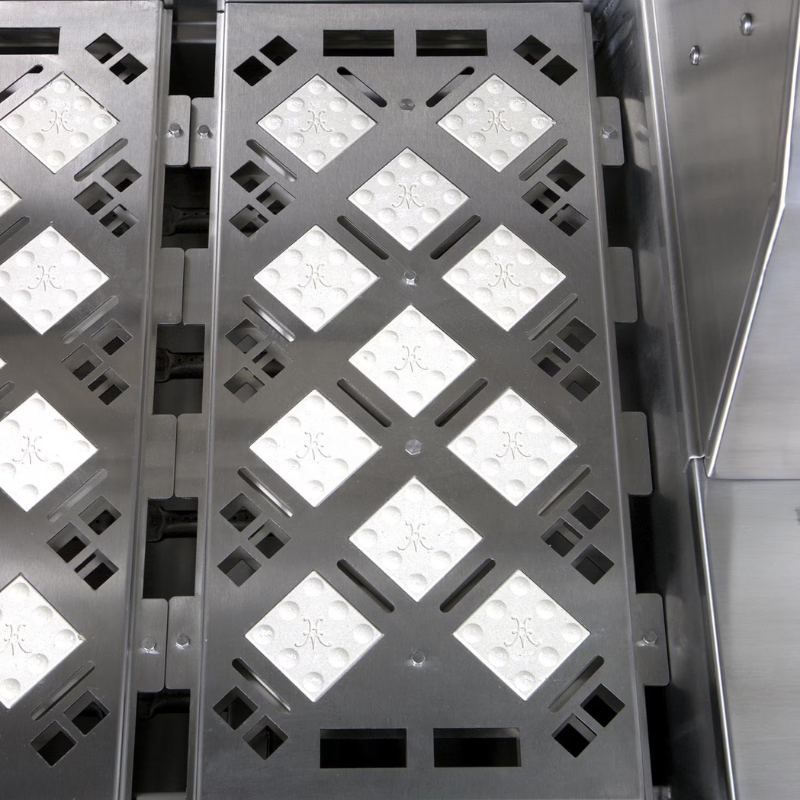 Close-up of a metallic grill with a patterned surface featuring diamond shapes and circular designs, suitable for cooking or grilling applications.
