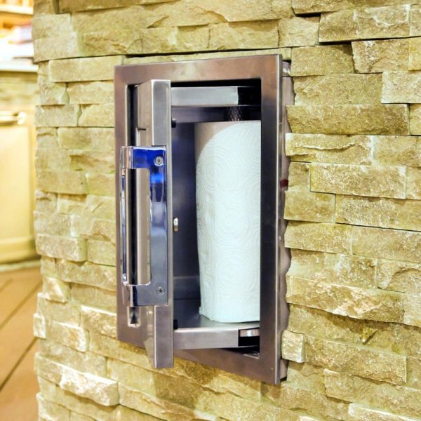 Stainless steel paper towel dispenser mounted on a textured stone wall, providing convenient access for cleaning and kitchen use.