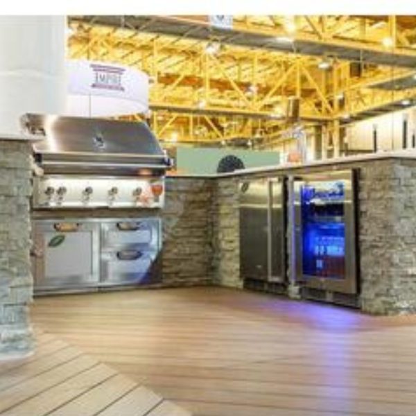 Outdoor kitchen setup featuring a stainless steel grill and beverage cooler with stone cabinetry and wooden flooring. Ideal for entertaining and cooking outdoors.