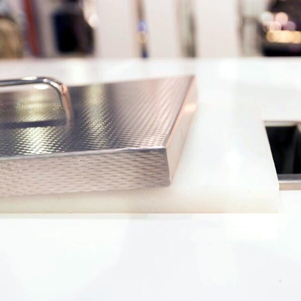 Close-up of a textured stainless steel lid resting on a white cutting board, highlighting modern kitchenware design.