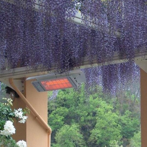 Outdoor infrared heater installed under a pergola adorned with purple wisteria flowers, surrounded by lush greenery.