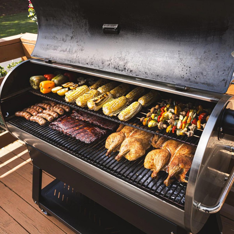 Grilled meats and vegetables on a barbecue grill, featuring chicken, sausages, corn, and vegetable skewers, showcasing outdoor cooking.