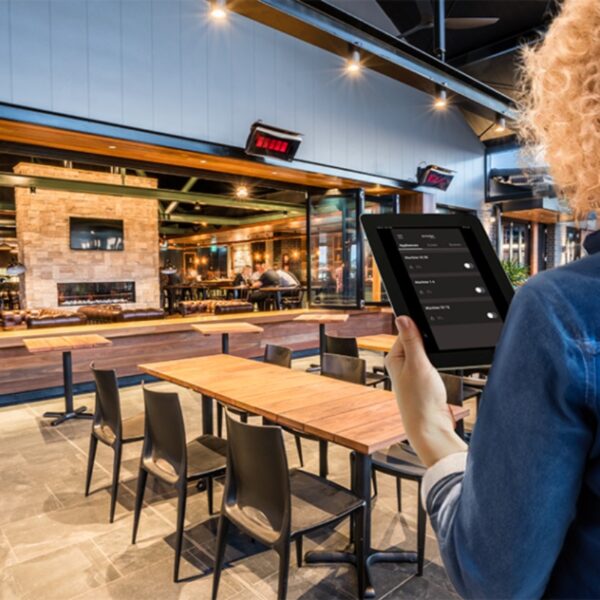 A person using a tablet to manage settings in a modern restaurant with wooden tables and an inviting atmosphere.