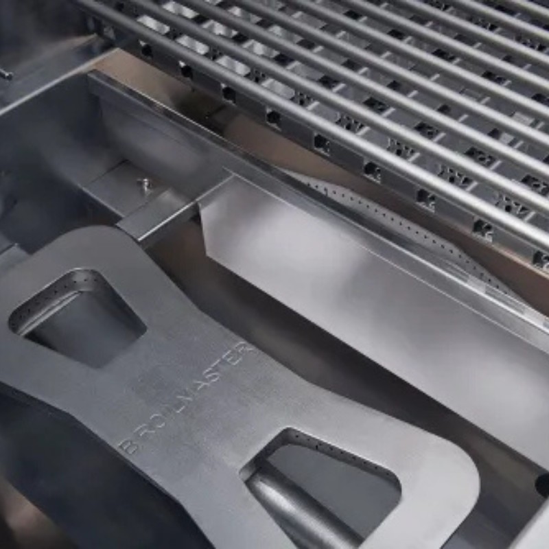Close-up view of a stainless steel grill featuring adjustable grates and a Broilmaster cooking accessory, highlighting its durable design for outdoor cooking.