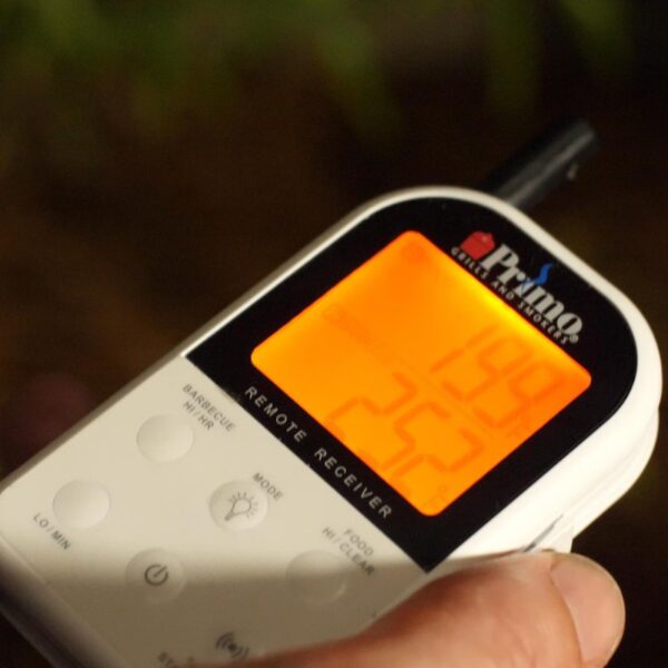 Digital meat thermometer displaying temperature readings for barbecue and food, held in a hand.