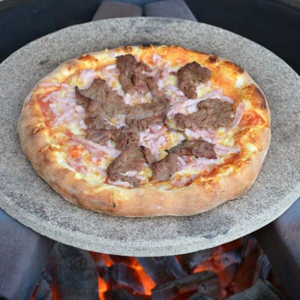 Stone-cooked pizza topped with beef and ham, placed on a hot cooking surface over glowing coals.