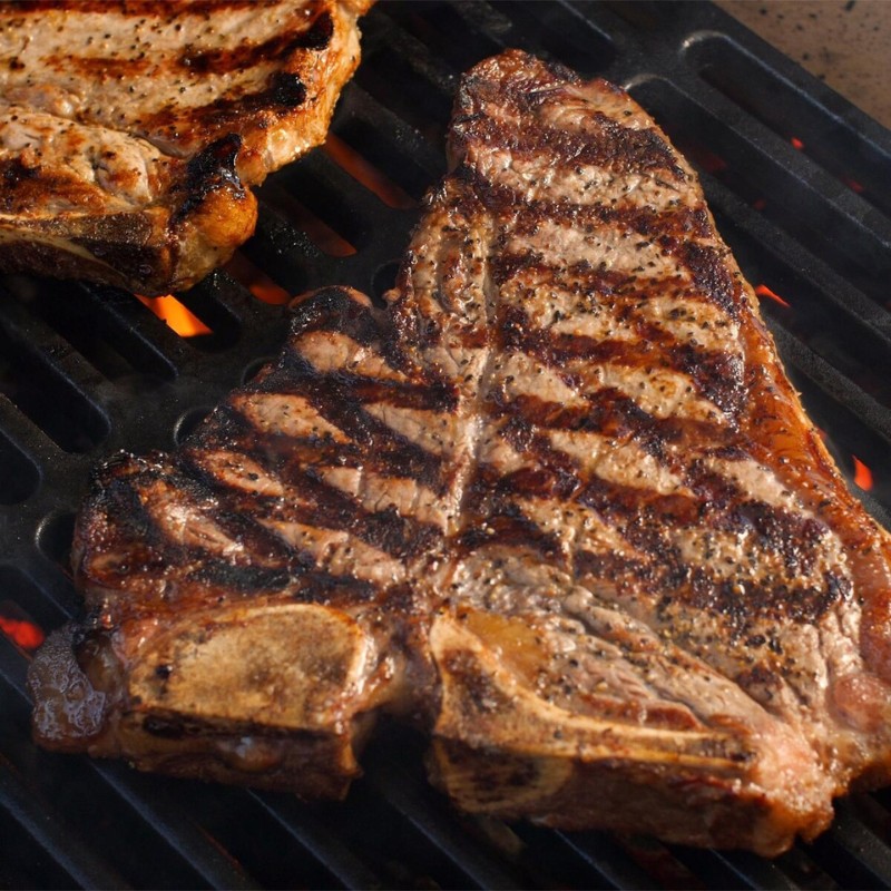 Grilled steaks with distinct char marks cooking on a barbecue grill over glowing coals.