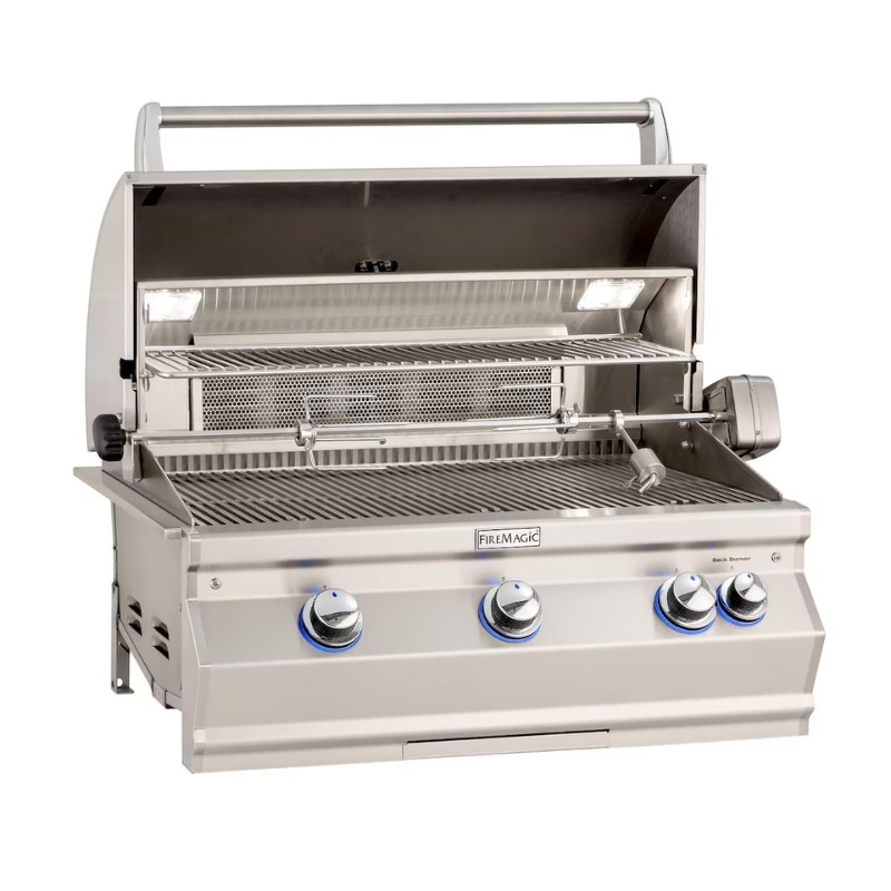 Stainless steel Fire Magic outdoor gas grill with an open lid, featuring three control knobs, an adjustable warming rack, and built-in lighting for nighttime grilling.