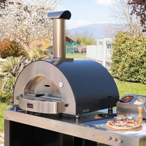 Outdoor pizza oven on a stainless steel cart, featuring a curved black exterior and smoke chimney, with a freshly made pizza and condiments nearby.
