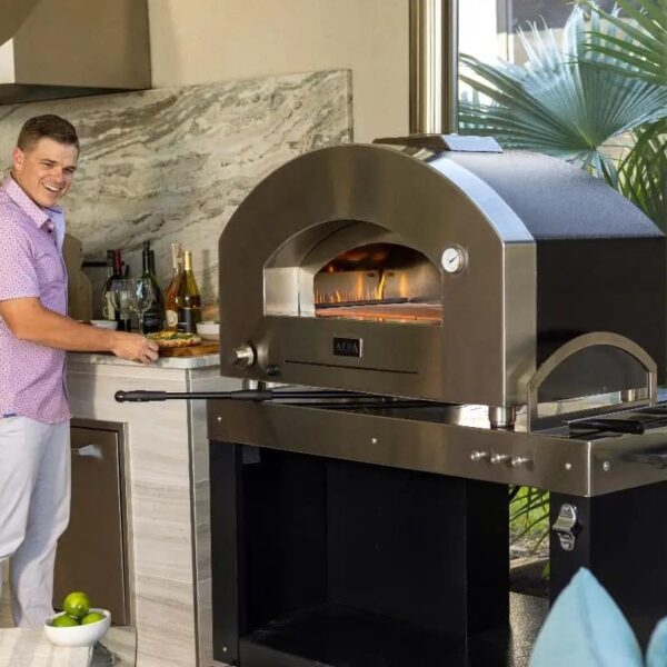 Man preparing food near a modern outdoor pizza oven, set in a stylish kitchen with drinks and limes on the counter.