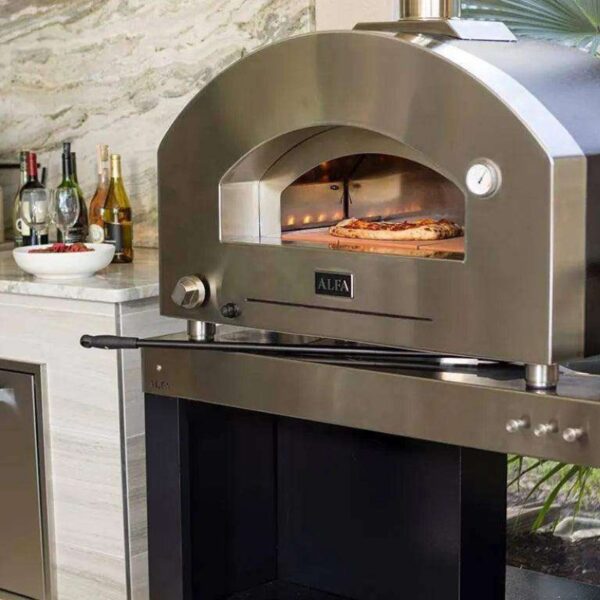 Stainless steel outdoor pizza oven with a visible pizza baking inside, situated in a modern kitchen setting with drinks and appetizers on the countertop.