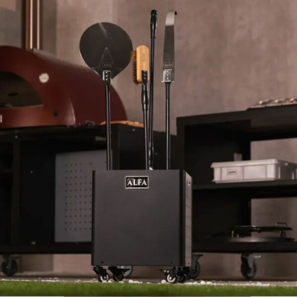 Black pizza oven toolset with a pizza peel, brush, and cutter, stored in a mobile holder labeled ALFA, set against a modern kitchen backdrop.