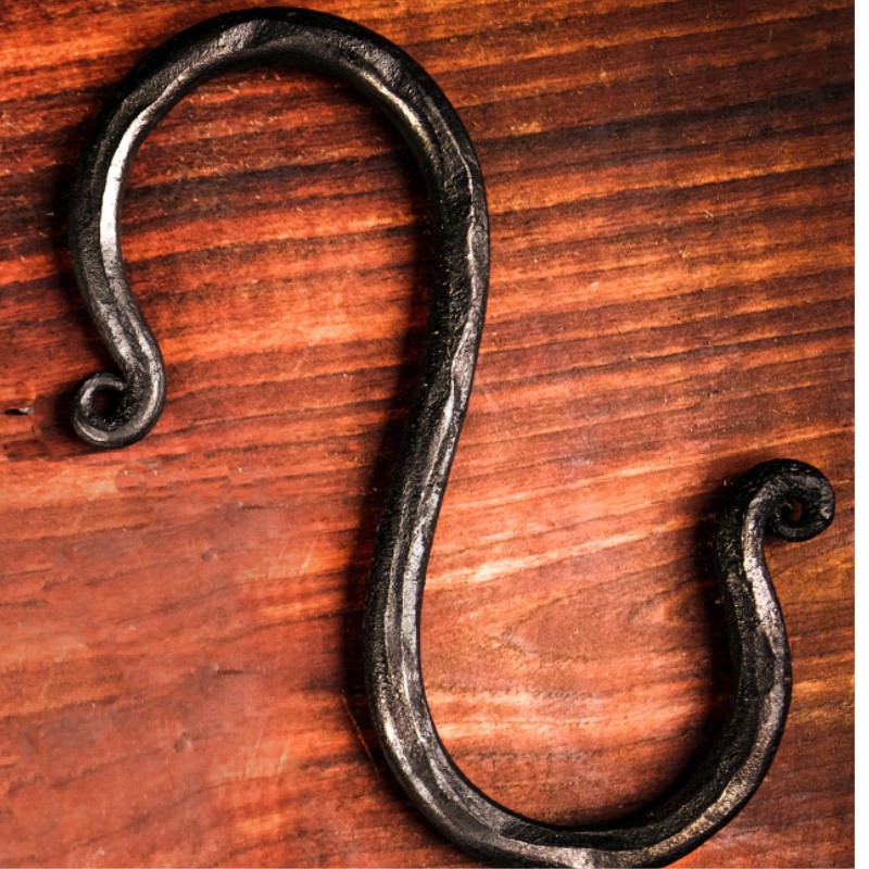 Black wrought iron s-hook on a wooden surface, showcasing a decorative twisted design and curved ends.