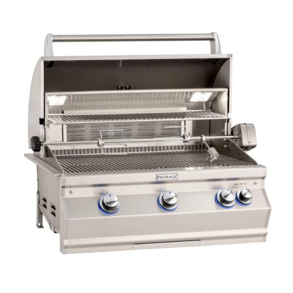 Stainless steel Fire Magic grill with open hood, featuring three control knobs, a warming rack, and interior lights.