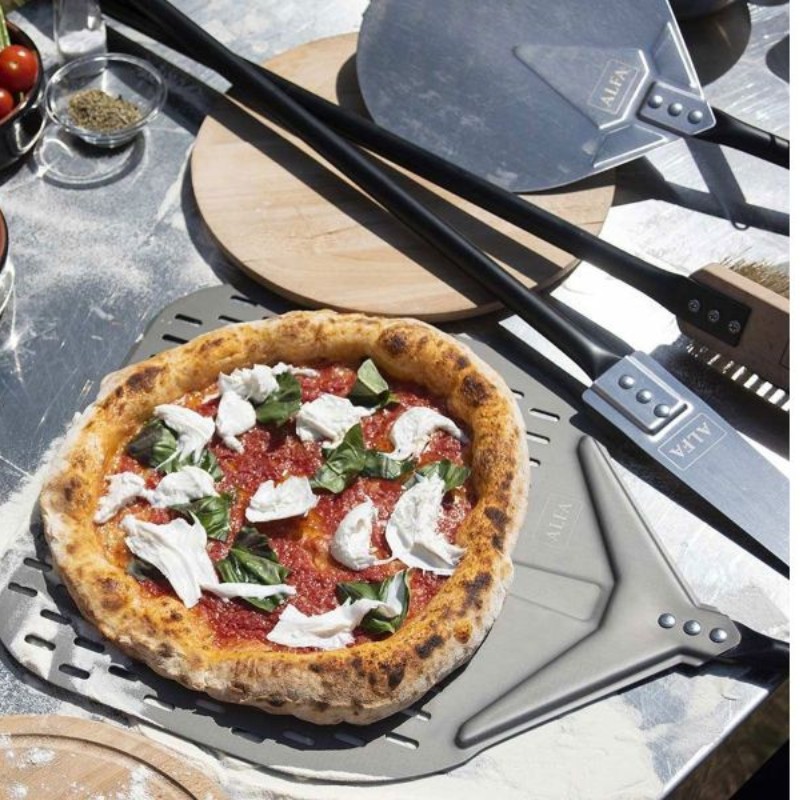 Freshly baked pizza topped with mozzarella and basil on a metal pizza peel, surrounded by kitchen tools and fresh ingredients.