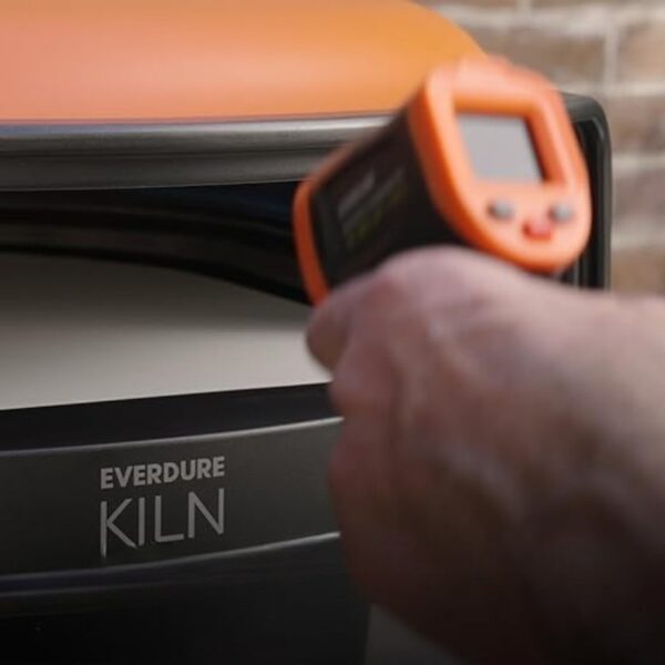 Hand holding a digital thermometer aimed at an Everdure Kiln, with the kiln's logo visible.