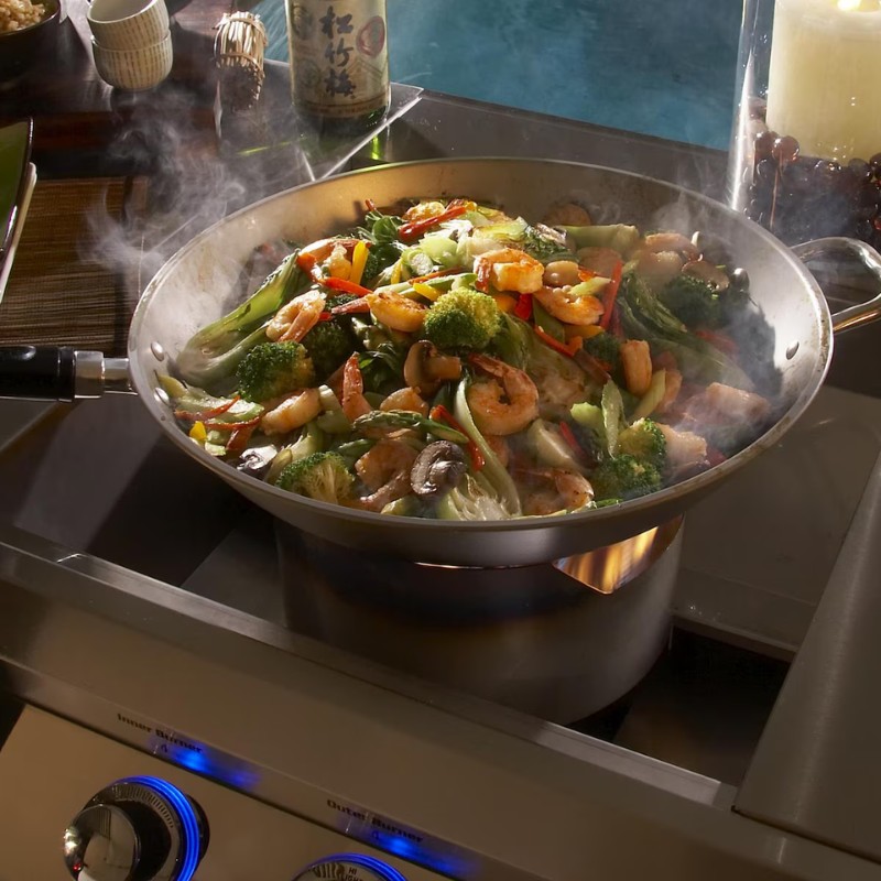 Stir-fried shrimp and vegetables including broccoli, bell peppers, and asparagus in a stainless steel pan, with steam rising and a modern stove in the background.
