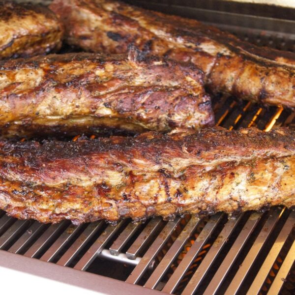 Grilled marinated pork ribs cooking on a barbecue grill, showcasing a golden-brown color and charred texture.
