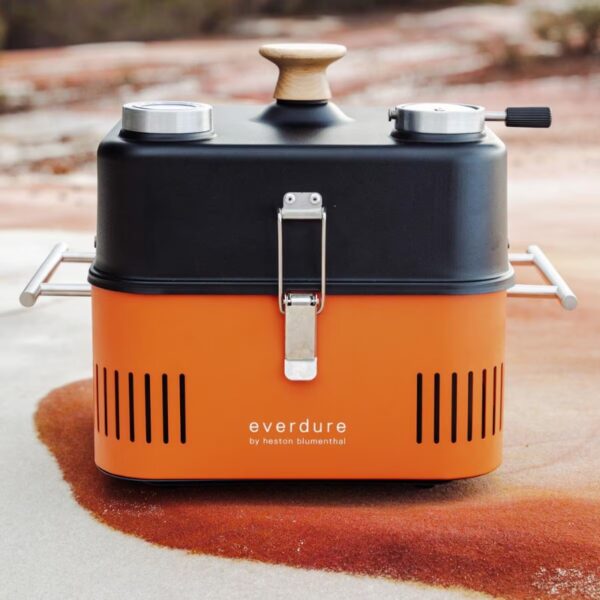 Portable orange charcoal grill with a black top and wooden knob, featuring two metal burners and a sturdy design, ideal for outdoor cooking.