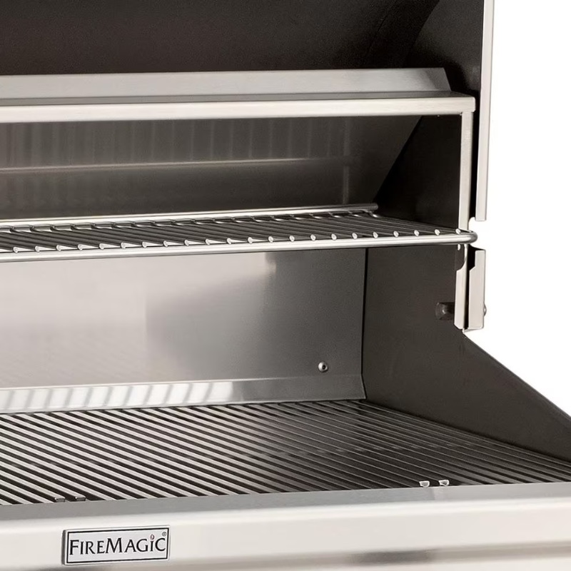 Interior view of a Fire Magic stainless steel gas grill with multiple cooking racks and a smooth griddle surface, designed for outdoor cooking.