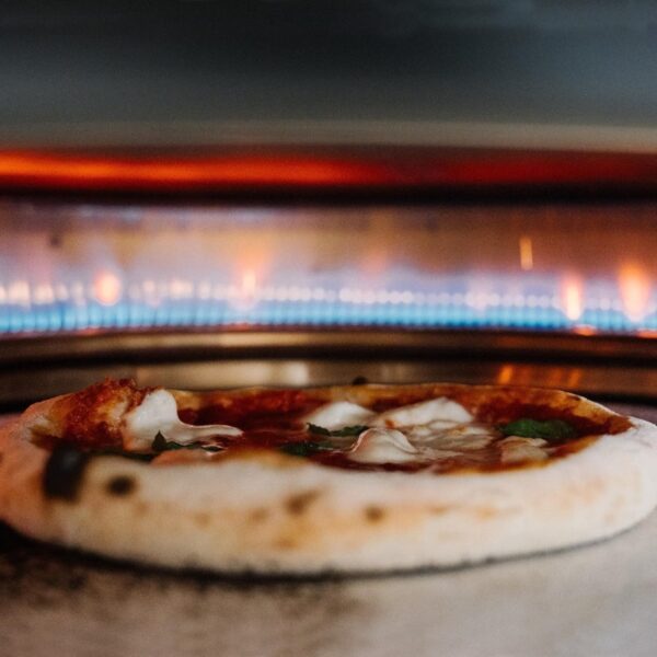 Pizza baking in a wood-fired oven with melted cheese and fresh basil on top.