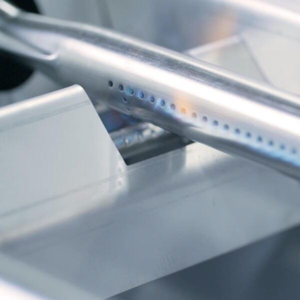 Close-up of a shiny metal component with perforations, likely part of a gas burner or grill, highlighting its design and functionality.